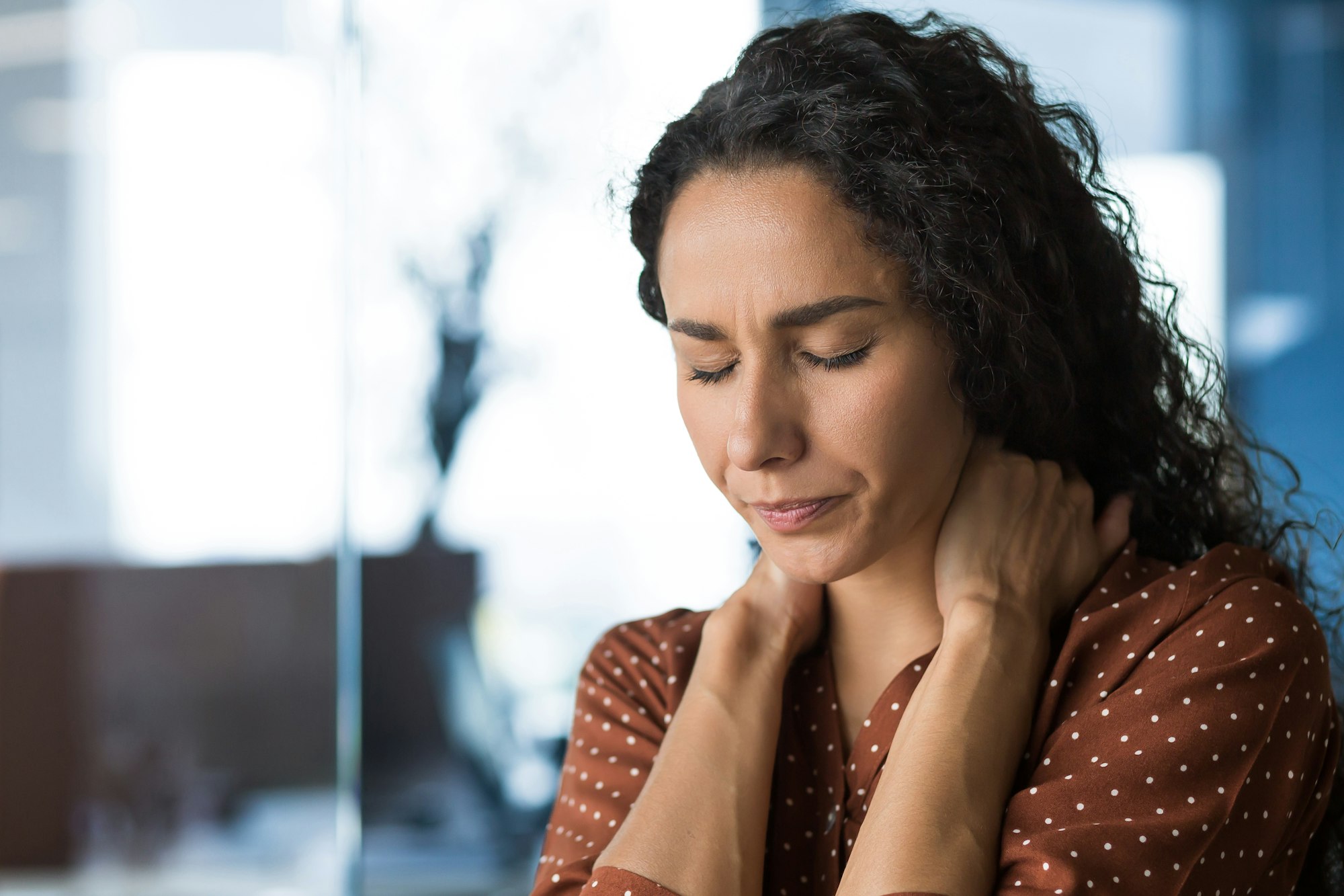 Hispanic woman overtired working in modern office businesswoman has severe neck pain, massages neck