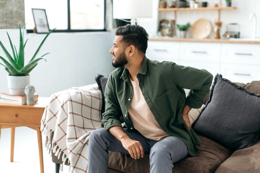 Problems with the back, spine, sciatica. Sad Arabian or Indian man, dressed in casual wear, sitting